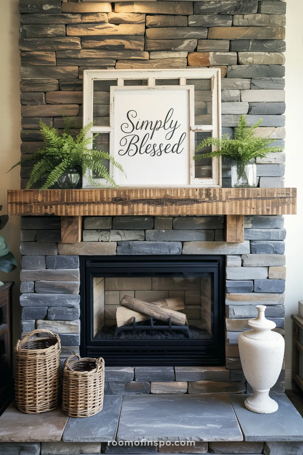 Farmhouse stone fireplace with a rough-hewn mantel decorated with a framed "Simply Blessed" sign and two vibrant ferns in glass jars.
