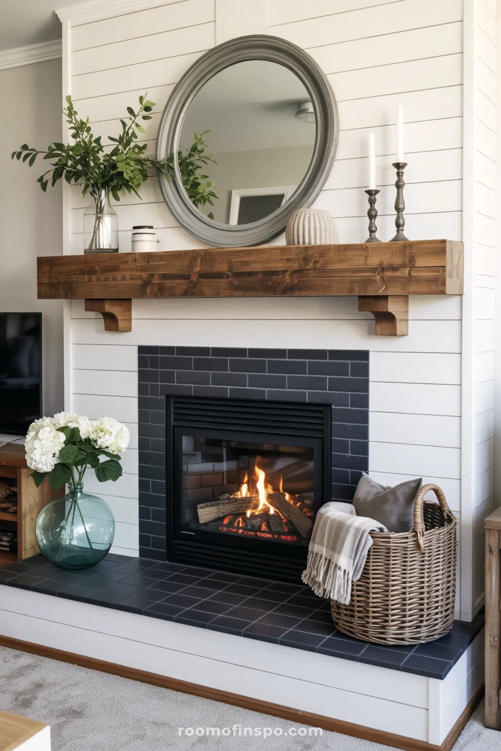 Farmhouse fireplace with shiplap and a dark tile surround, featuring a wood mantel with corbels, a round mirror, and candlesticks.
