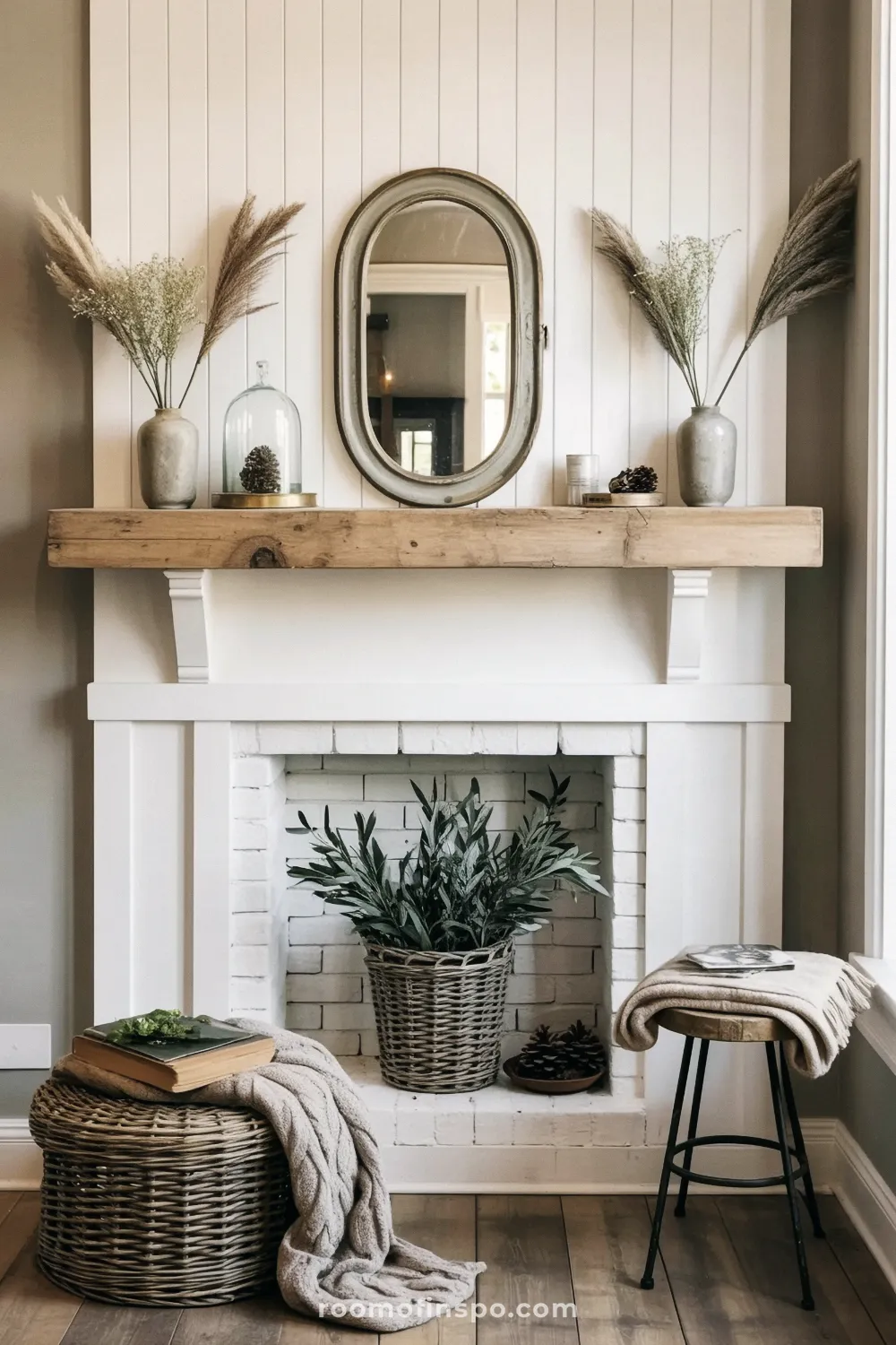 Farmhouse fireplace with shiplap and a white mantel with a rustic beam accent, holding an oval mirror and vases of dried pampas grass.