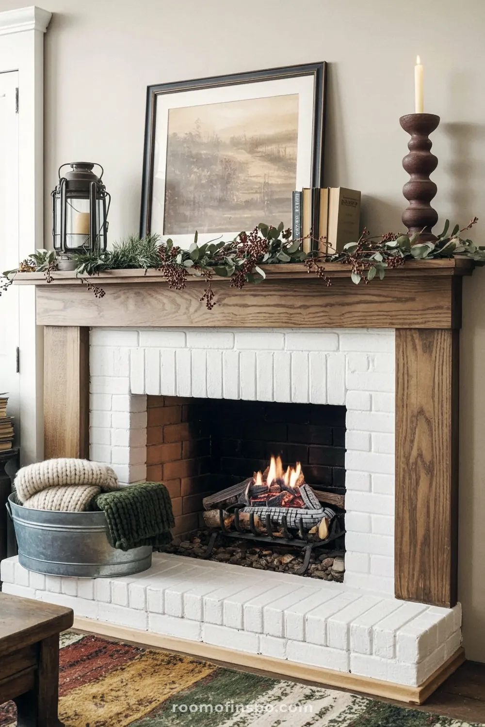 Farmhouse fireplace with white painted brick and a rustic wood mantel featuring a framed landscape print and a cranberry eucalyptus garland.
