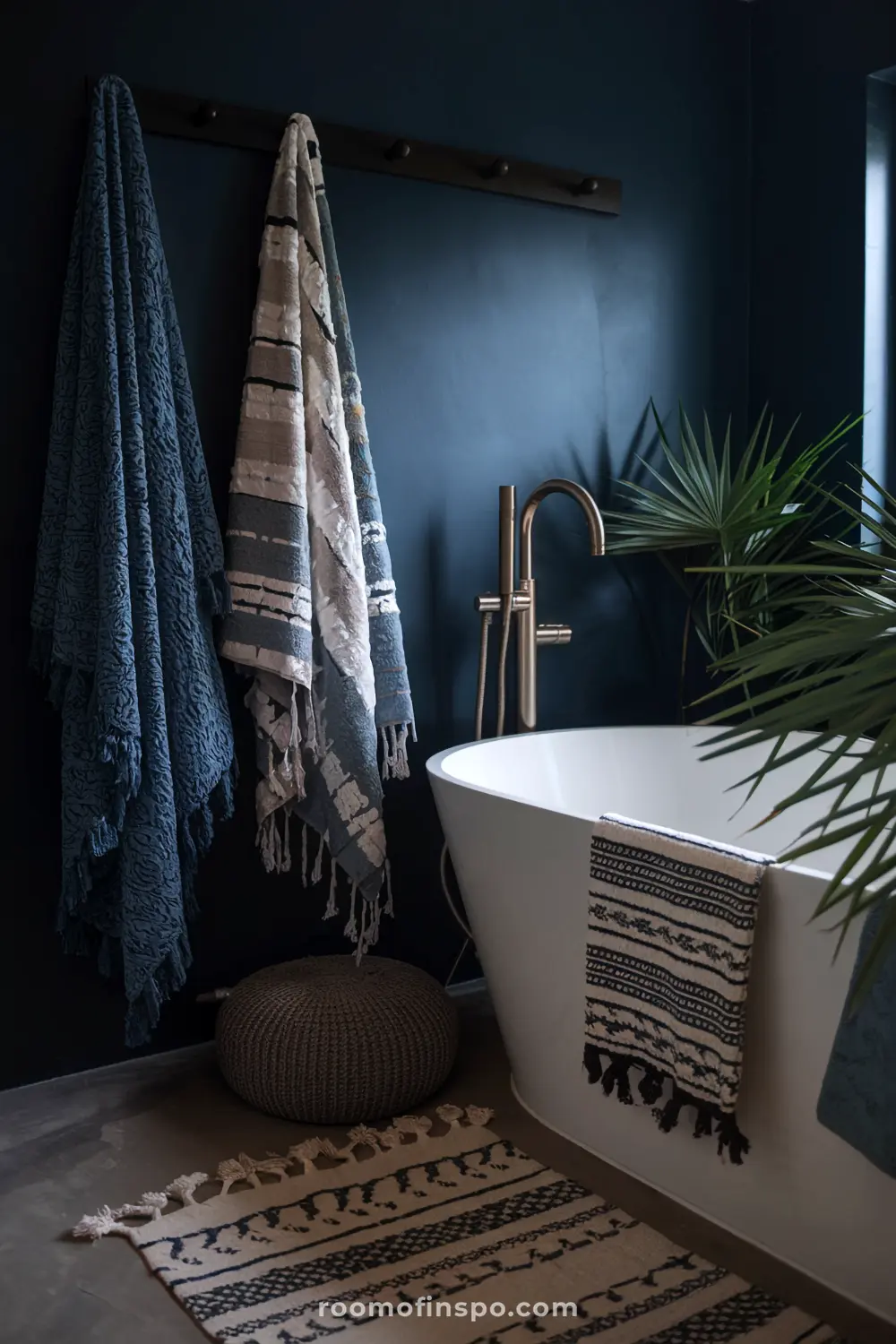 A moody bohemian bathroom with deep navy walls, gold fixtures, and a modern tub, creating a cozy and dramatic retreat.