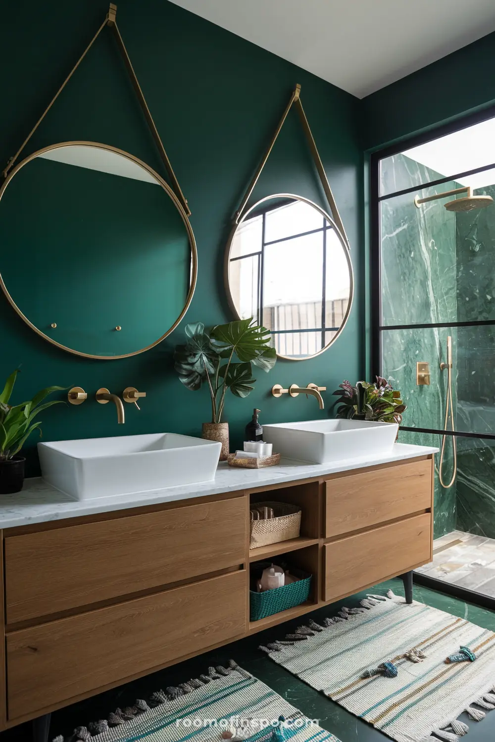 A boho-style bathroom interior with deep emerald green walls, two large round mirrors and a wooden vanity cabinet with white marble countertops.