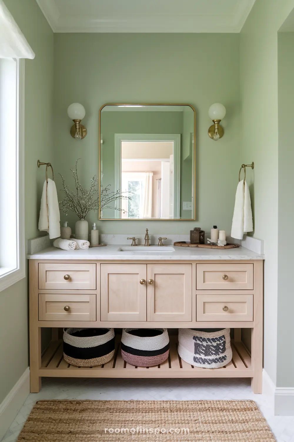 A bohemian bathroom with sage green walls, a light wood vanity, and brass accents for a soothing, natural feel.
