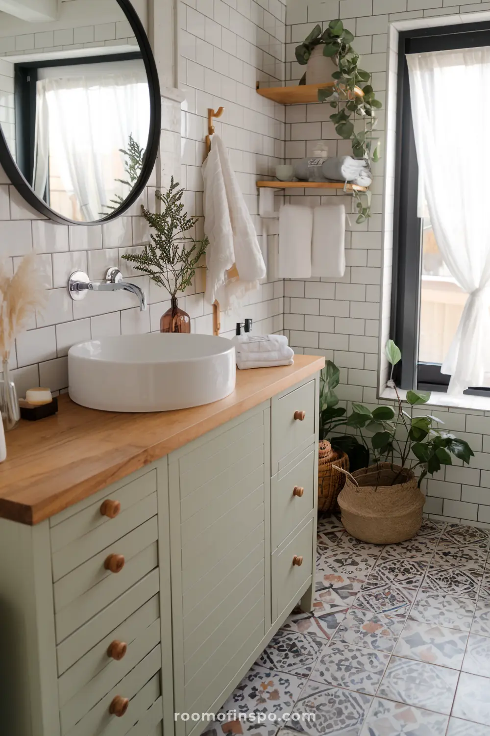 A farmhouse-boho bathroom with a wooden countertop, a light sage green farmhouse style cabinet and boho-style accessories.
