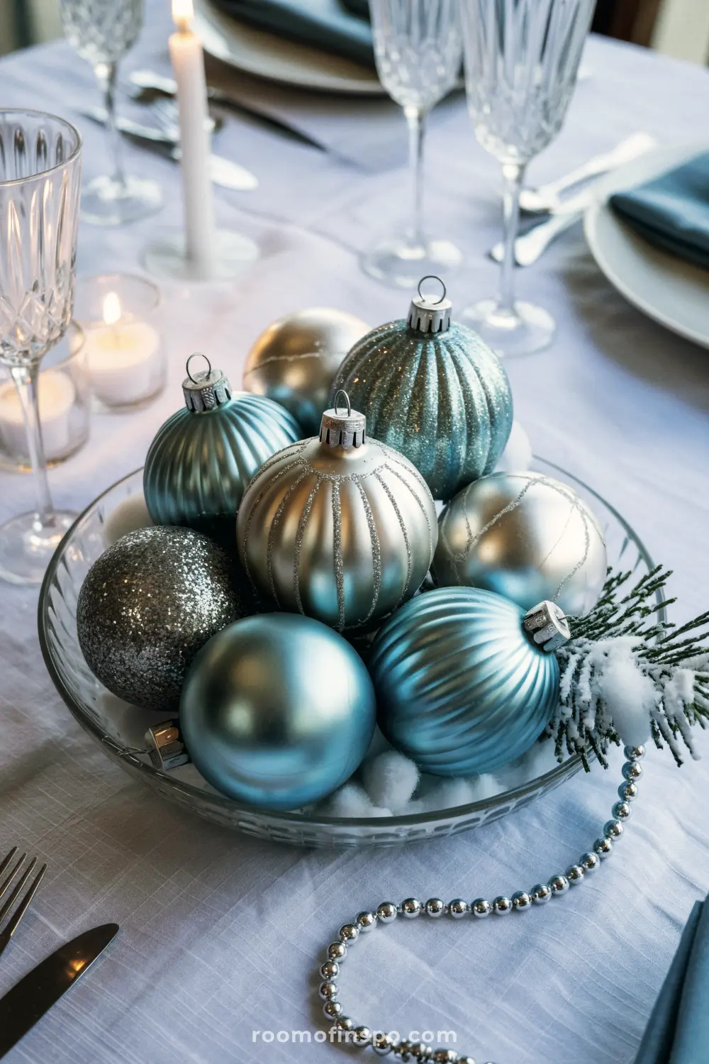 A serene and classy Christmas centerpiece of blue and silver ornaments in a clear bowl on a white tablecloth.