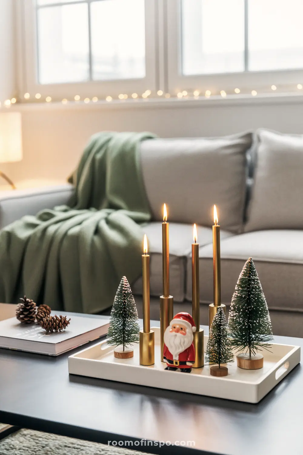 A white tray displays tall gold candles, a tiny Santa, and miniature trees, signifying a yearly tradition of yuletide joy.