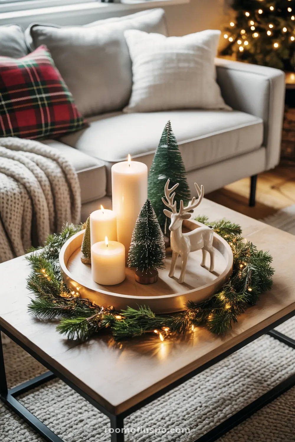 A styled yearly centerpiece displays a complex arrangement of candles, miniature trees, and a reindeer figurine on a wooden coffee table.