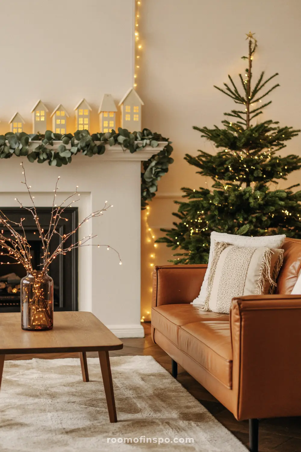 A charming and classy Christmas living room with a small, decorated tree and glowing white ceramic houses on the fireplace mantel.