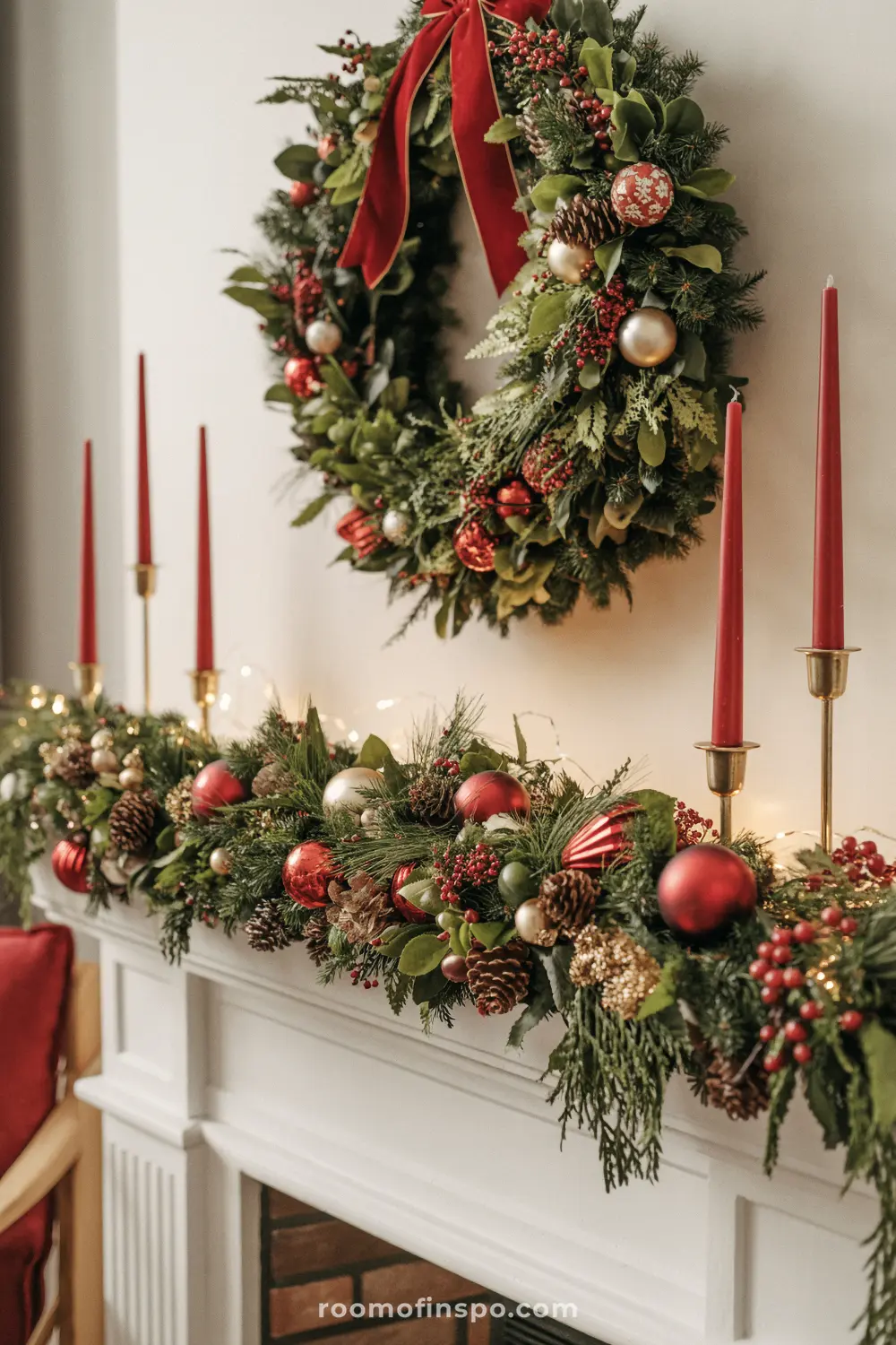 A festive, traditional Christmas mantel featuring a garland of greenery, red ornaments, pinecones, and tall red taper candles.