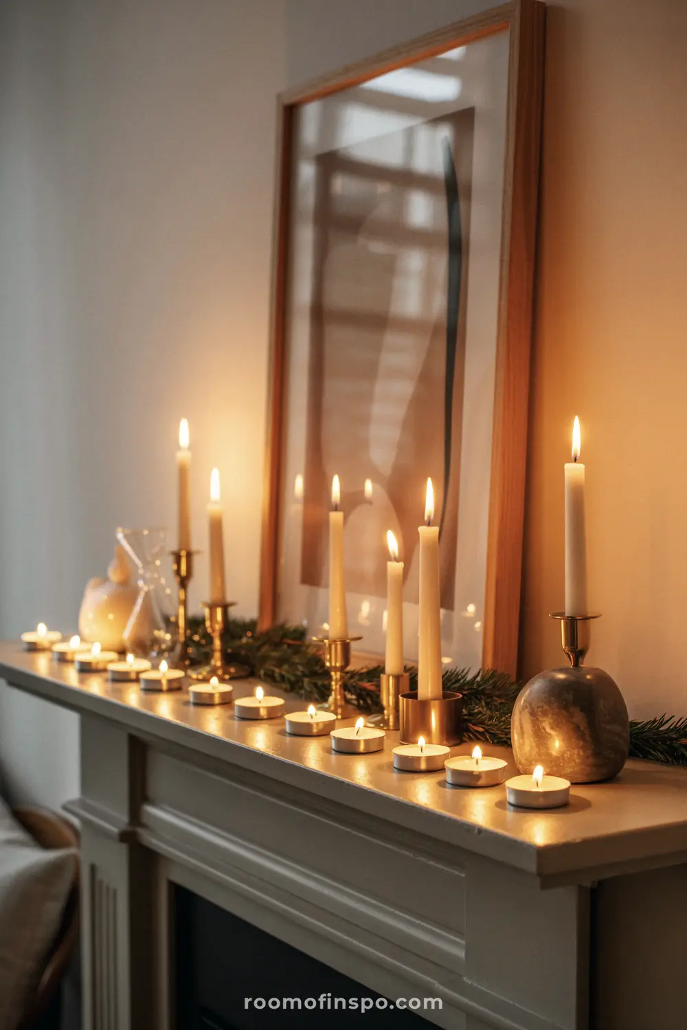A soft, warm Christmas mantel covered in a dozen lit candles and tea lights on gold stands with sparse greenery.