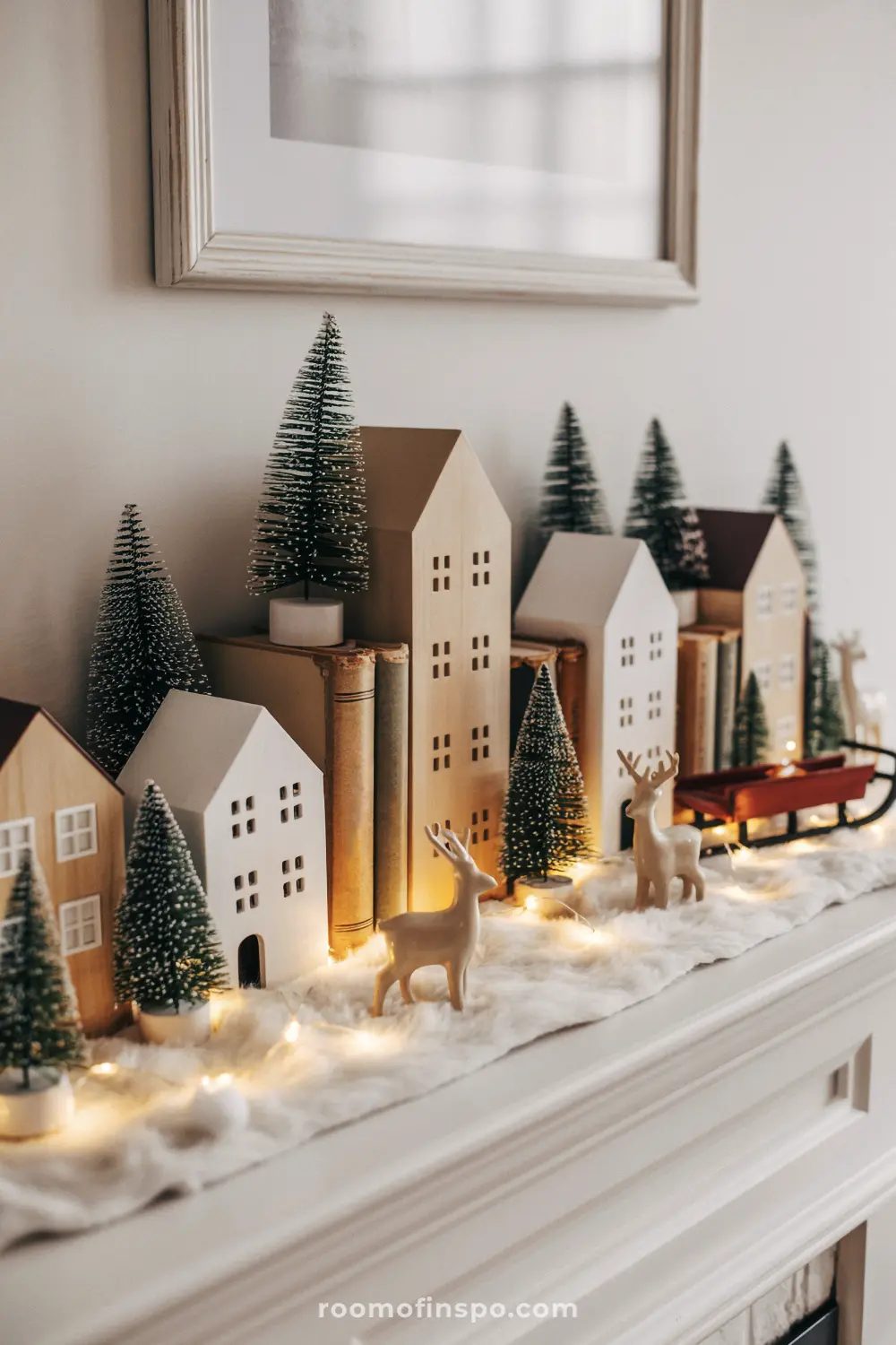 A charming Christmas mantel village with rustic wood houses, ceramic reindeer, bottle brush trees, and soft lighting.