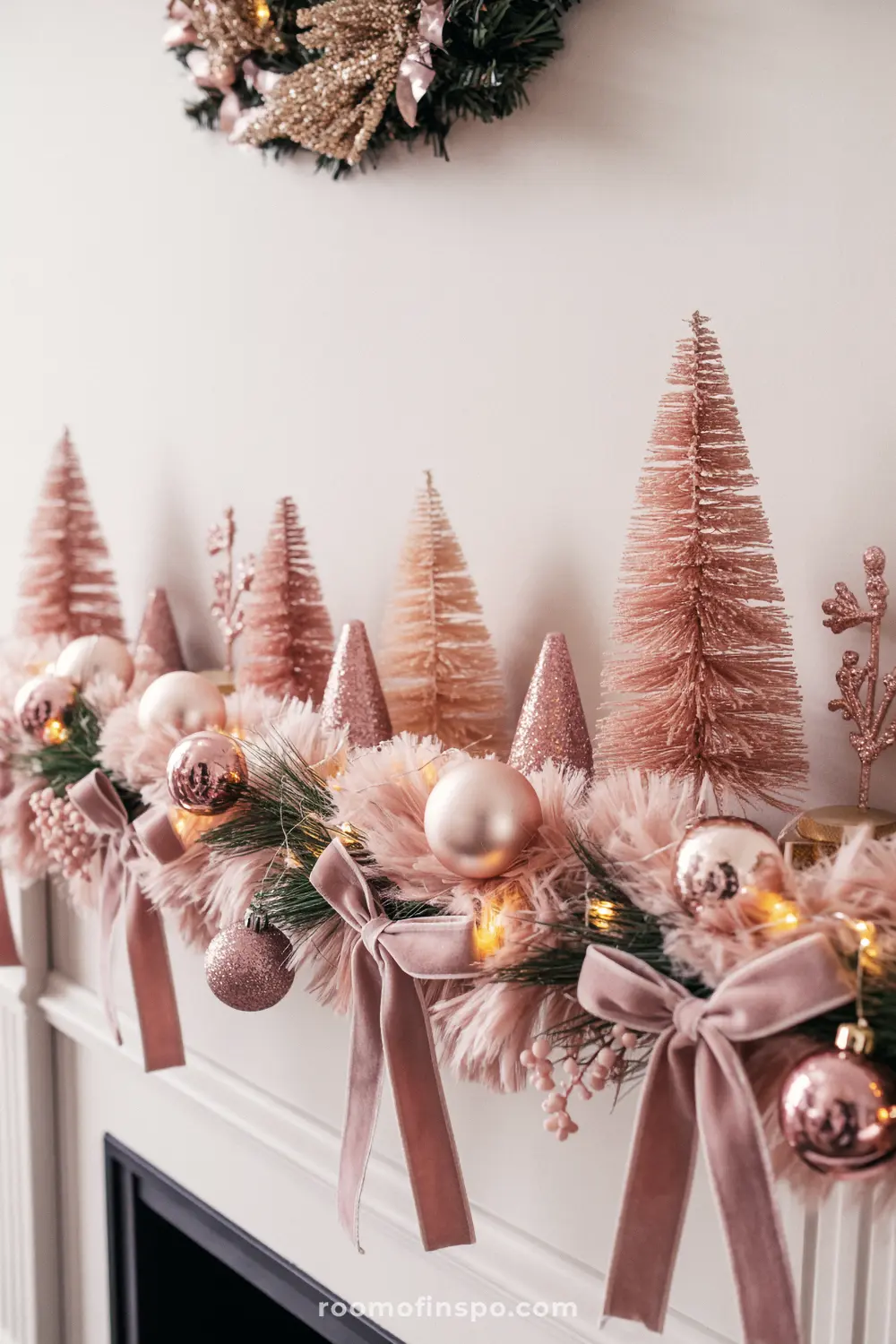 A charming pink Christmas mantel with bottle brush trees, soft pink garland, velvet bows, and matte pink ornaments.