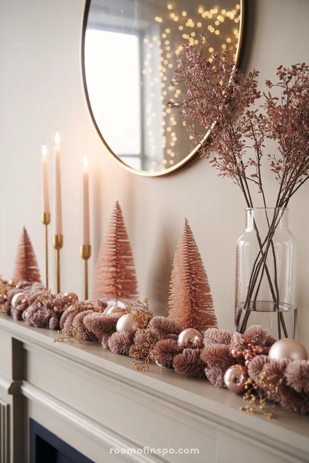 A modern pink Christmas mantel featuring tapered candles, blush bottle brush trees, and a thick, cozy, pink pom-pom garland.