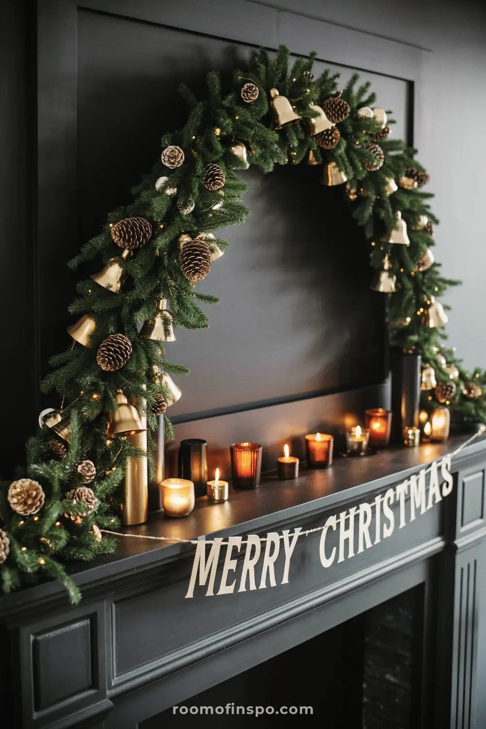 A moody, dramatic Christmas mantel with a black background, a bell garland, and multiple glowing votive candles.