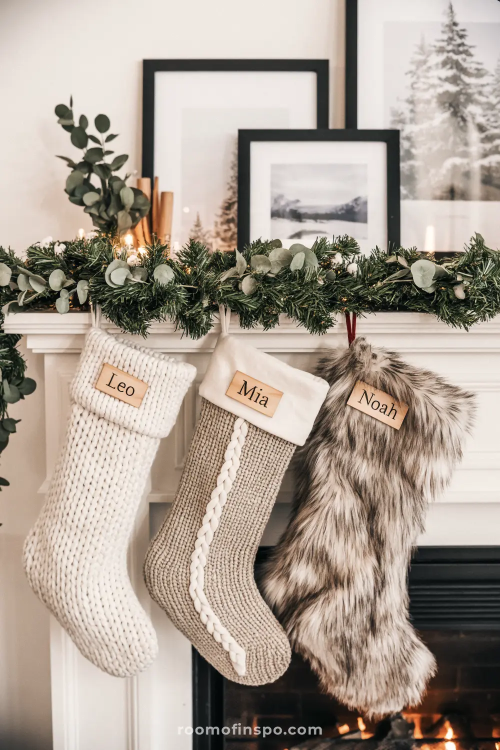 A neutral, textured Christmas mantel with knitted and faux-fur stockings featuring personalized name tags hanging beneath a simple eucalyptus garland.