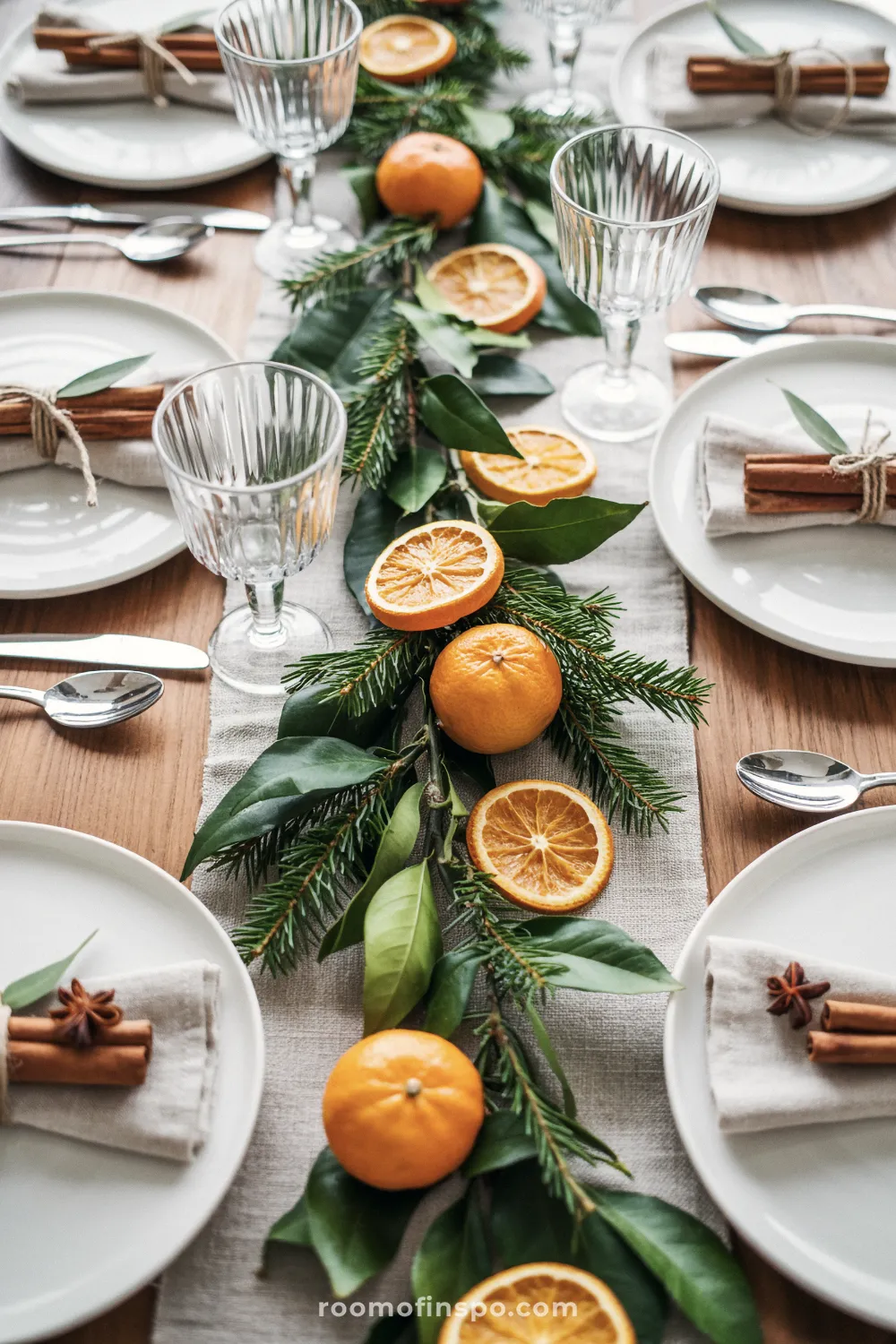 Fresh and natural Christmas table setting with a centerpiece of dried oranges, clementines, and greenery, complemented by cinnamon stick napkin ties.