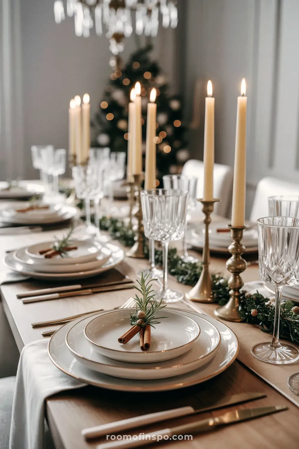 A beautiful and classy Christmas dinner table setting with tall, lit candles, garland, and cinnamon sticks on white plates.