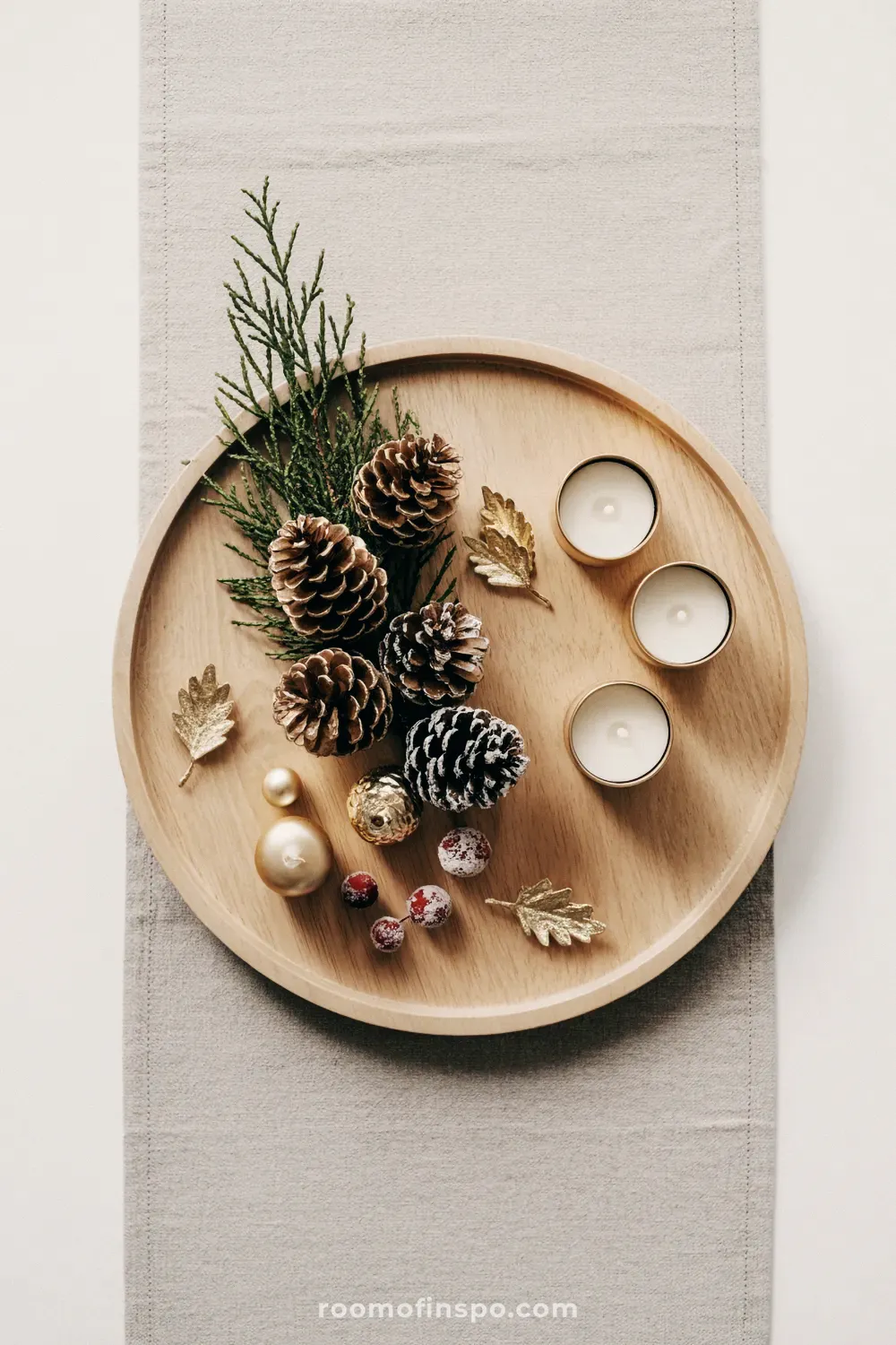A simple and classy Christmas centerpiece on a wooden tray with pinecones, gilded leaves, and frosted red berries.