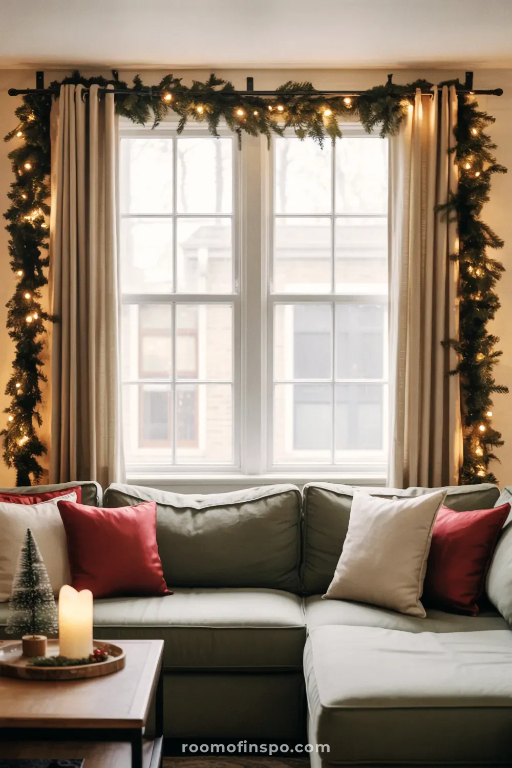 A warm and classy Christmas living room with a white sofa, red velvet pillows, and fairy lights framing the large window.