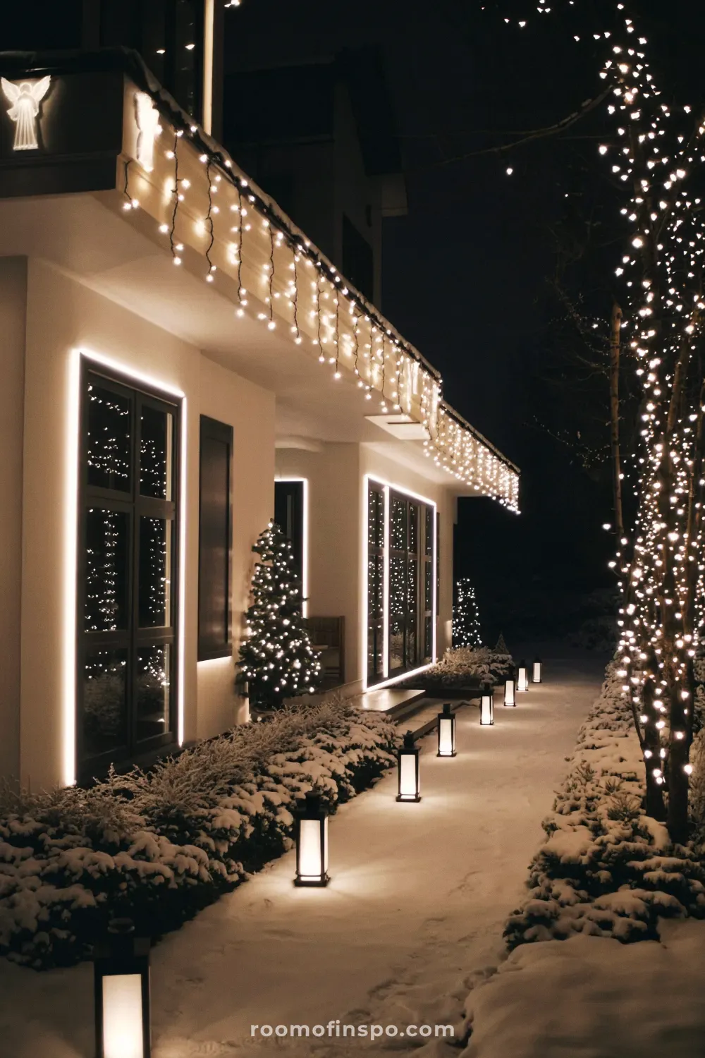 A modern and classy Christmas home with sleek linear lighting, icicle lights, and illuminated lanterns lining the snowy walkway.