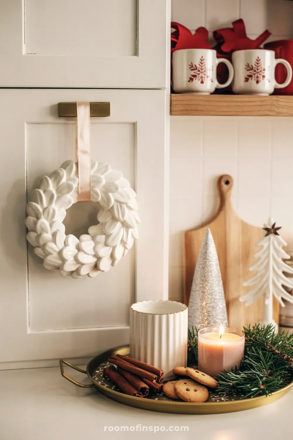 A cozy and classy Christmas kitchen with a white ceramic wreath, festive mugs, and a tray of cookies and cinnamon sticks.