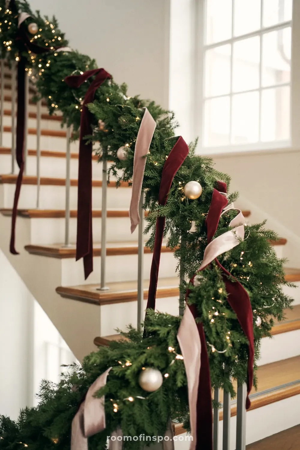 A gorgeous and classy Christmas staircase with lush evergreen garland, flowing blush velvet ribbons, and gold ornaments.