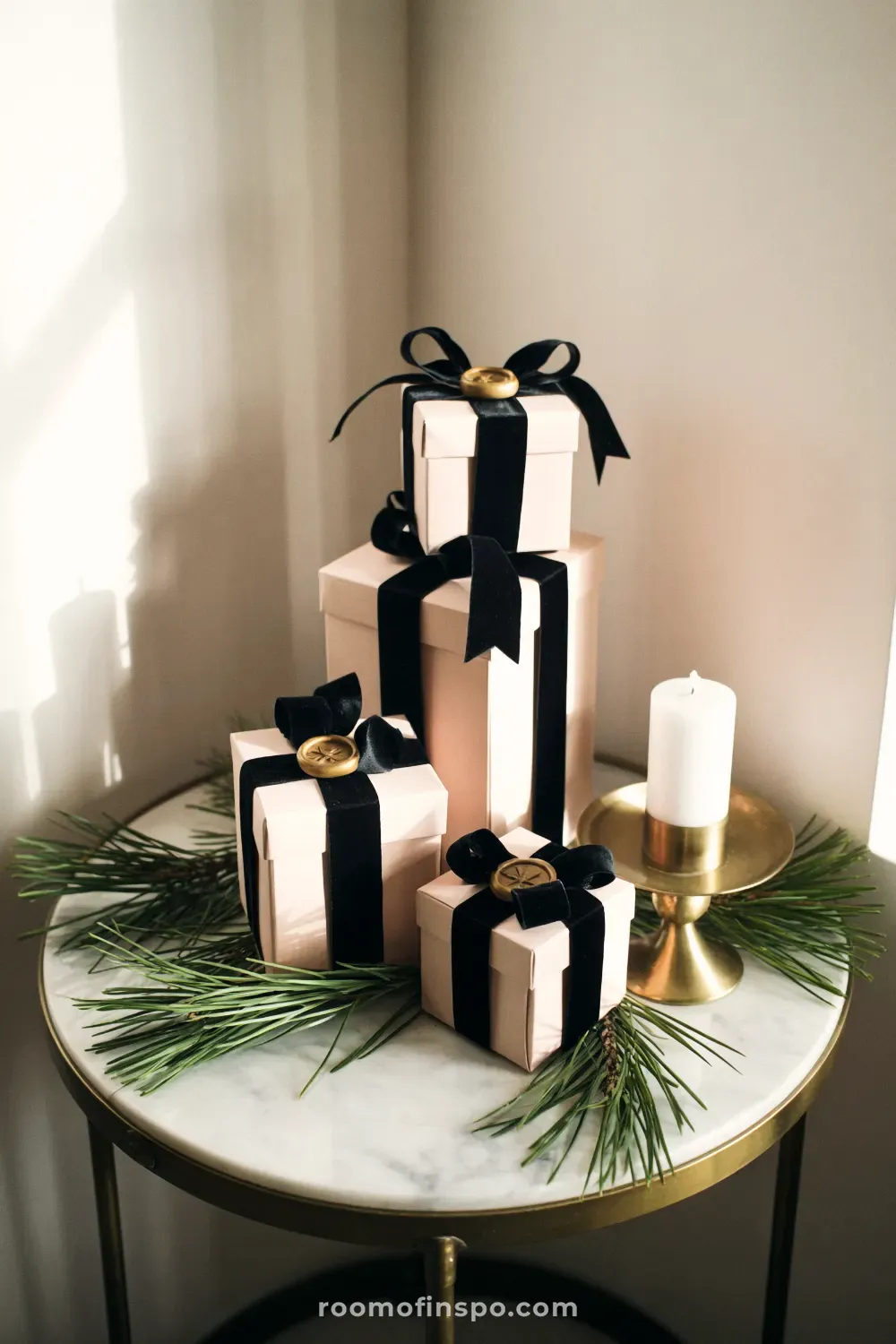 A chic and classy Christmas display of blush pink gifts with black velvet ribbons, pine sprigs, and a gold candle holder.