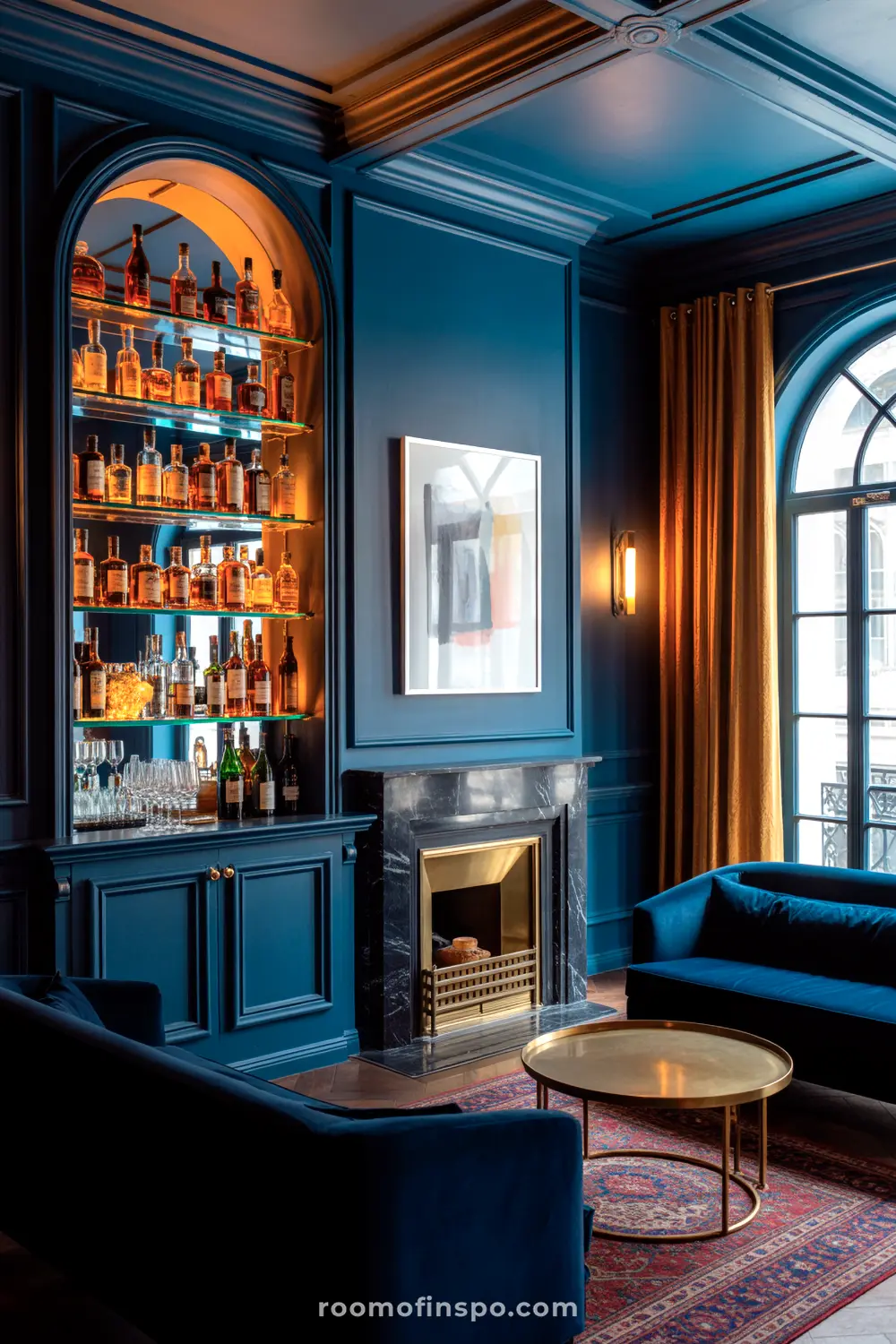 A Classy Man Cave with deep blue walls, a fully stocked bar with illuminated bottles, plush blue sofas, and a marble fireplace, exuding sophistication.