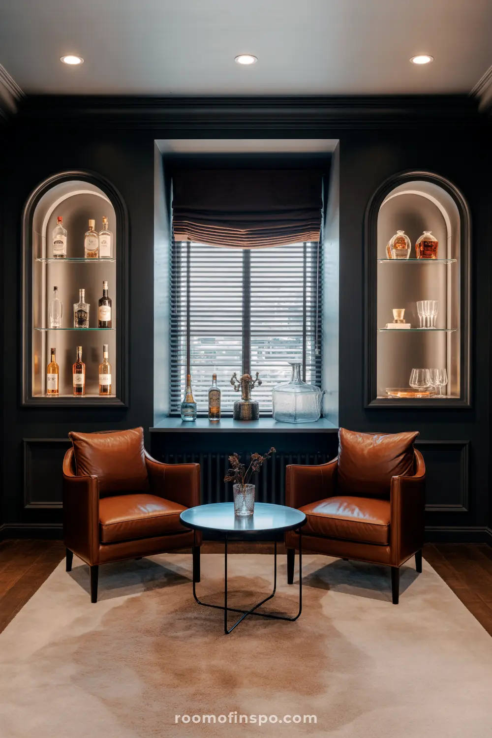 A Classy Man Cave featuring two brown leather armchairs, a round table, and arched display shelves with liquor bottles and glassware flanking a window.