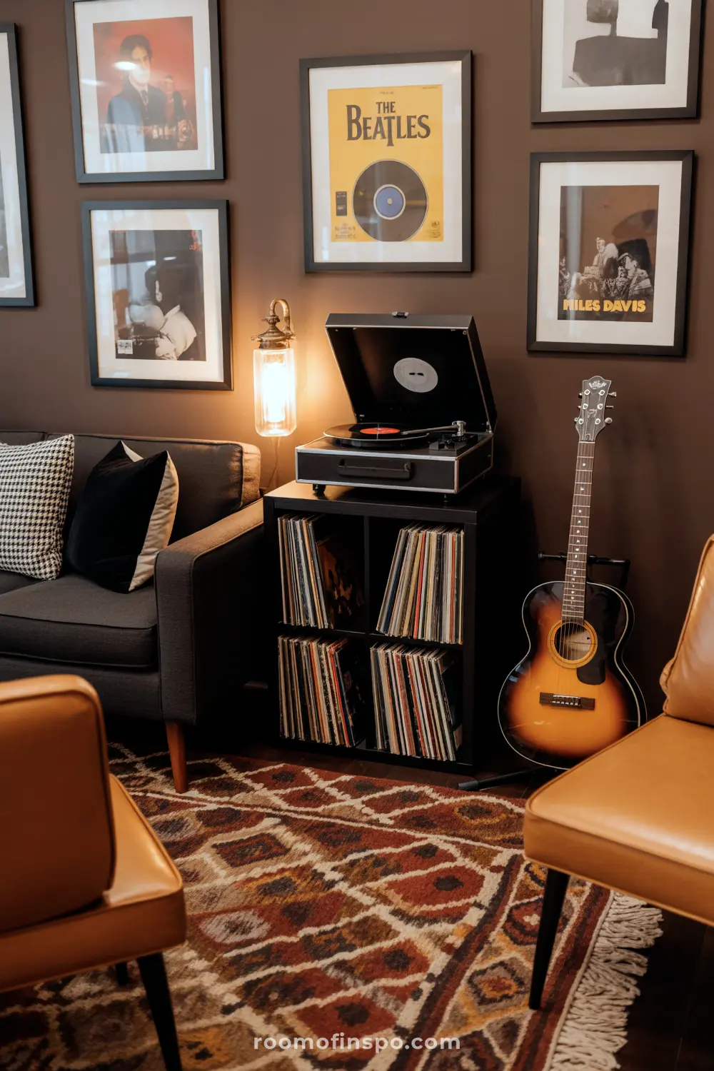 A Classy Man Cave music corner featuring a record player atop a vinyl collection, an acoustic guitar, and framed music posters on a dark wall.