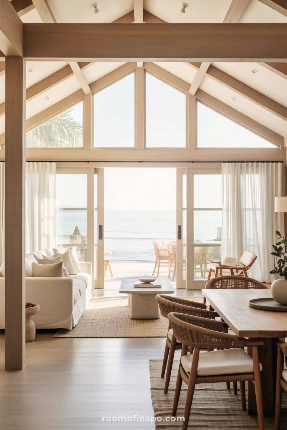 A coastal living room with double-height ceiling, exposed beams, and ocean view through floor-to-ceiling windows.