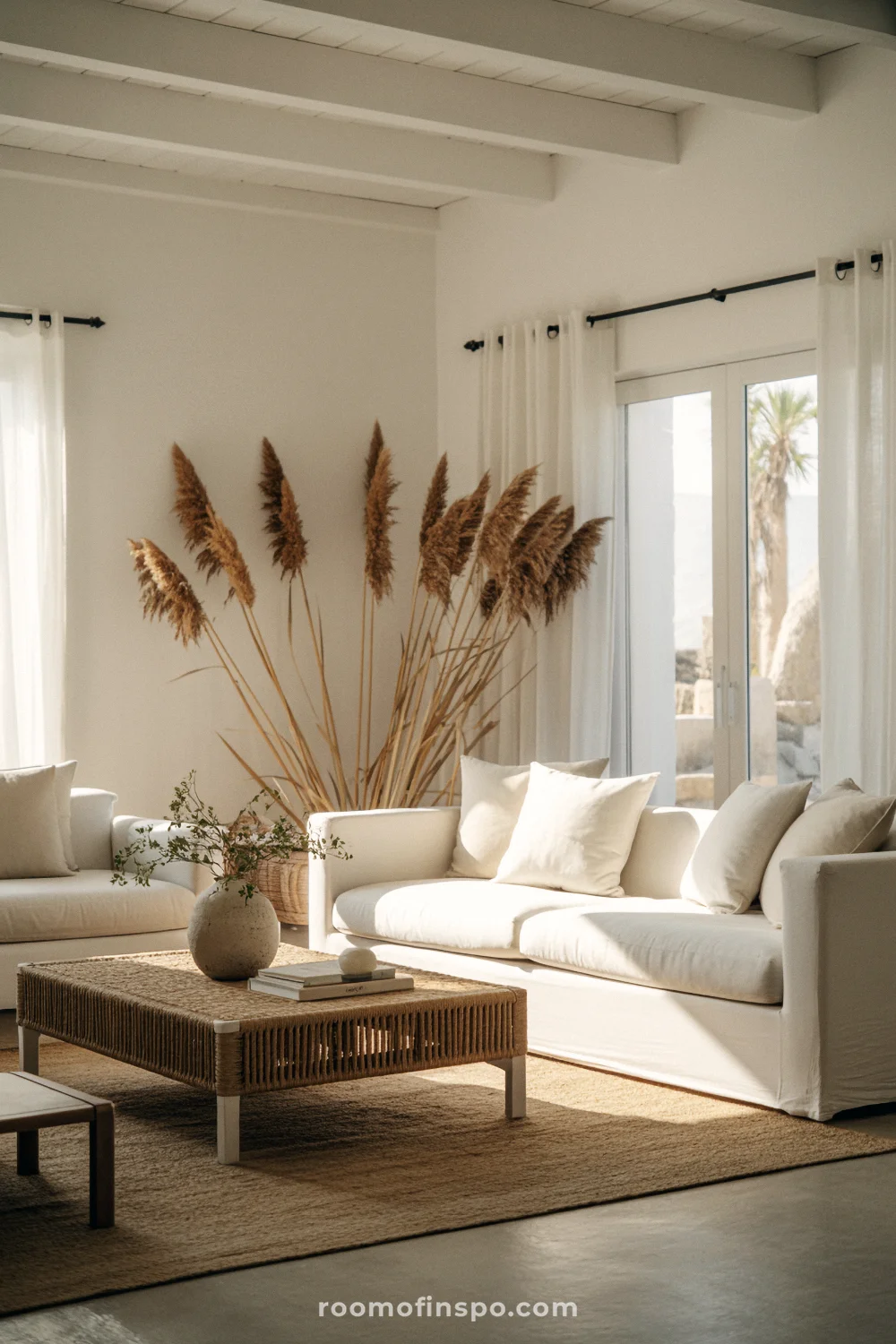 Serene coastal living room with white walls, organic materials, low-profile sofa, and pampas grass focal point.