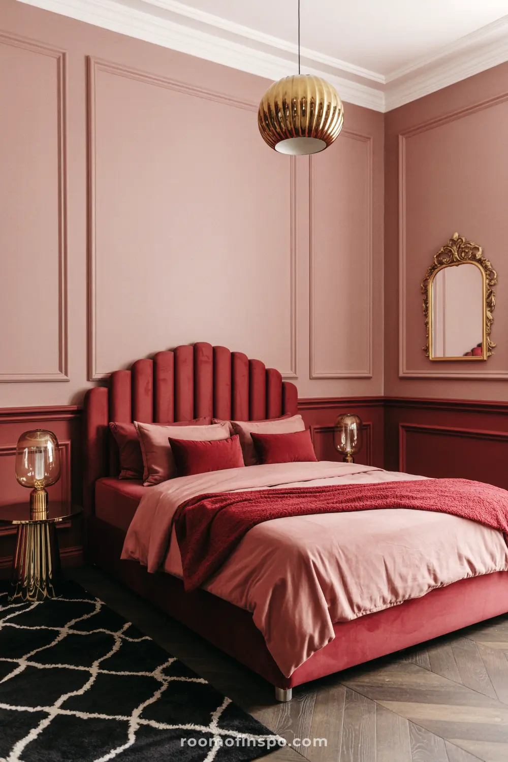 A moody, feminine bedroom with light pink walls, a dark red velvet bed, and a gold mirror and lamps.