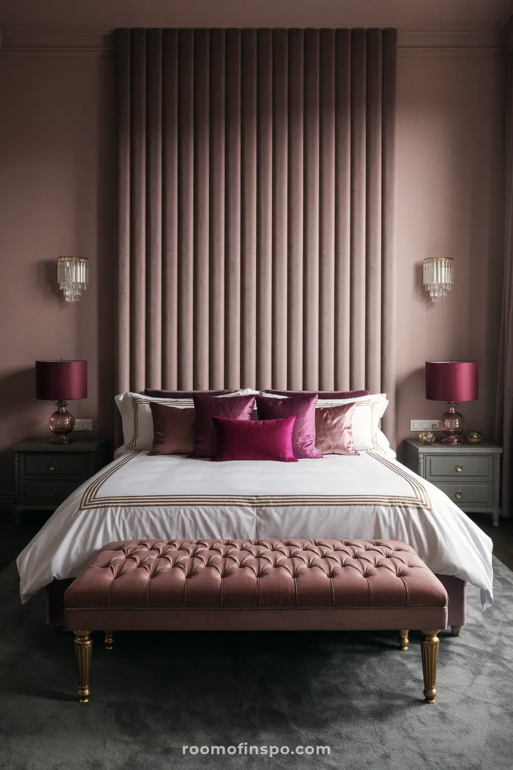 A dark, moody, and feminine bedroom with a tall plush headboard, berry-toned throw pillows, and pink lampshades.