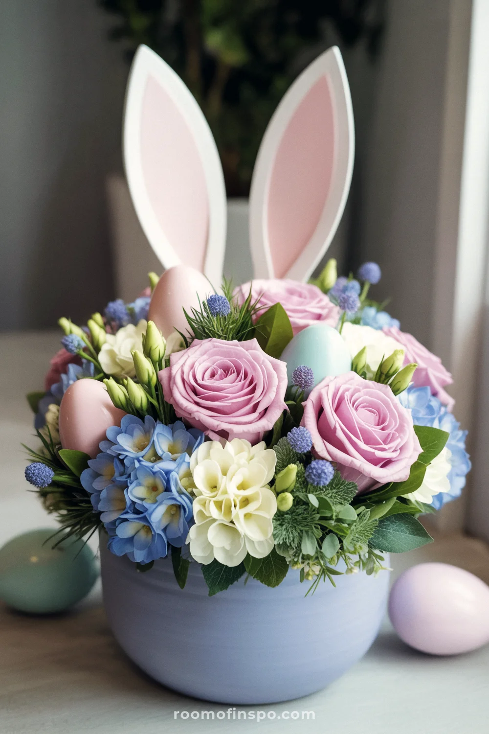 Pastel blue pot with pink roses, hydrangeas, bunny ears, and decorative eggs in a lush arrangement.