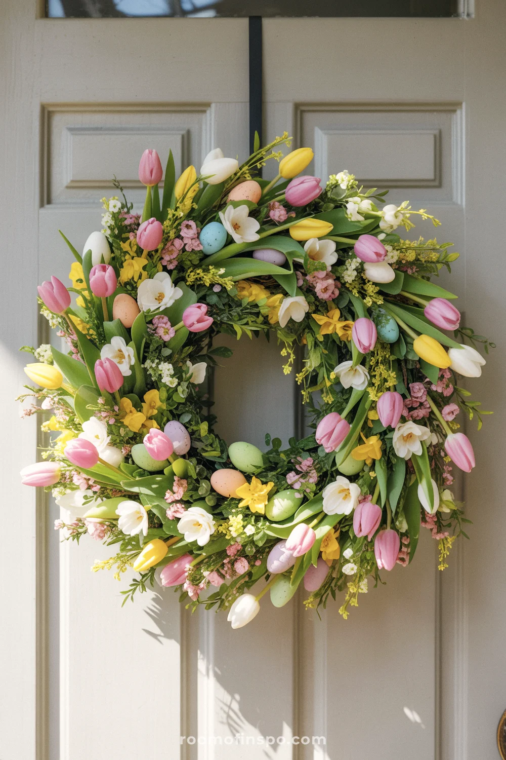A vibrant Easter wreath with spring florals and pastel eggs on a light gray door.