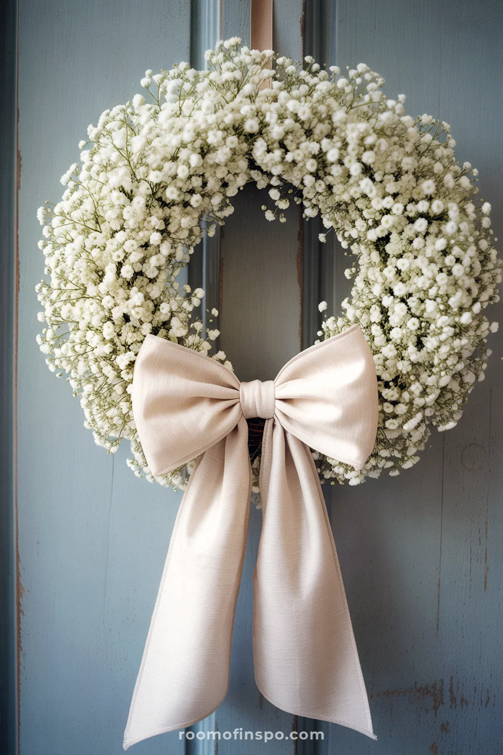 A neutral wreath with baby's breath flowers and a cream bow on a blue-gray door.
