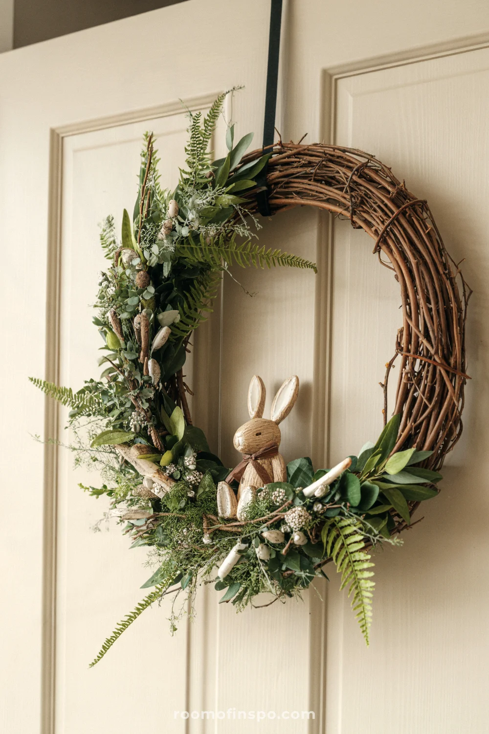 A rustic grapevine wreath with greenery and a small bunny on a white door.