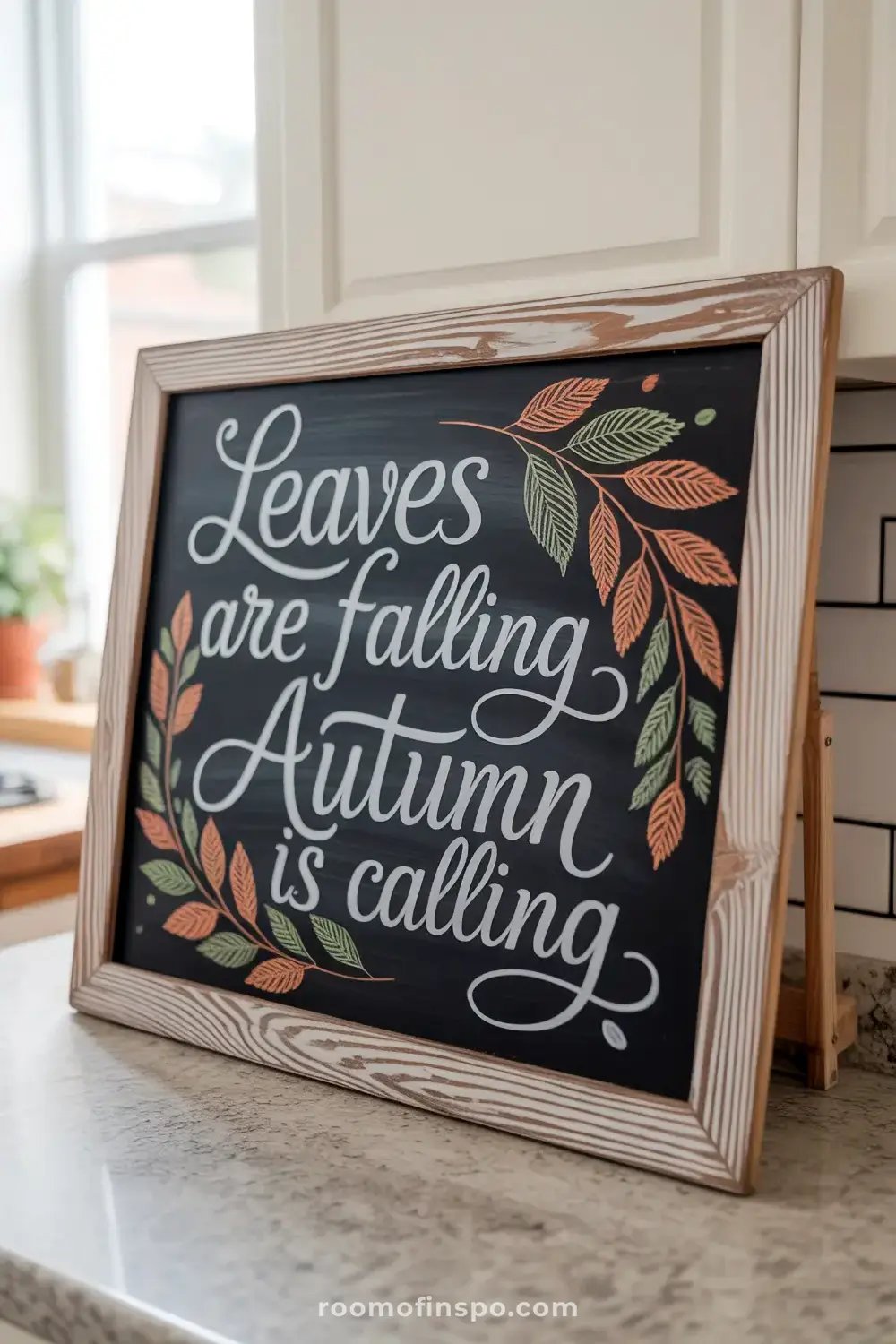 A framed chalkboard sign reads, "Leaves are falling, Autumn is calling," adorned with colorful sketched leaves.
