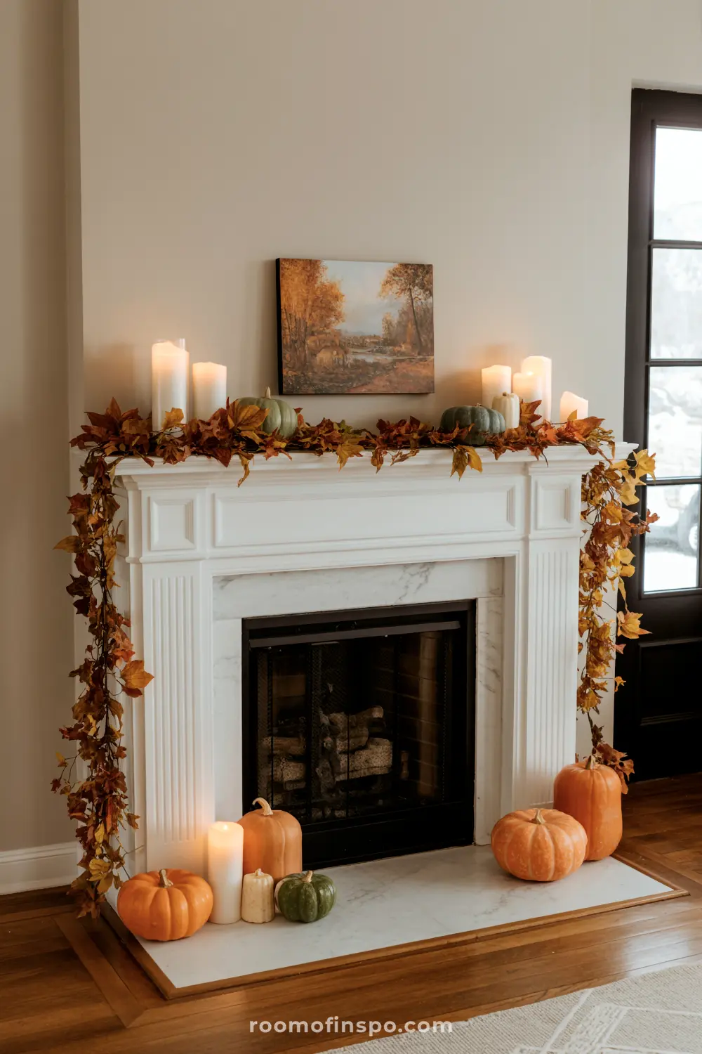 A traditional white mantel is beautifully decorated for autumn with a leafy garland, various pumpkins, and glowing candles, complementing a fall landscape painting.