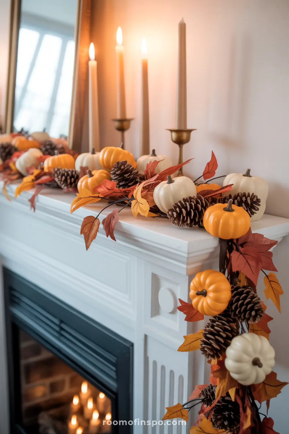 A classic white mantel is adorned with a festive fall garland of miniature pumpkins, pinecones, and colorful autumn leaves, illuminated by candles.