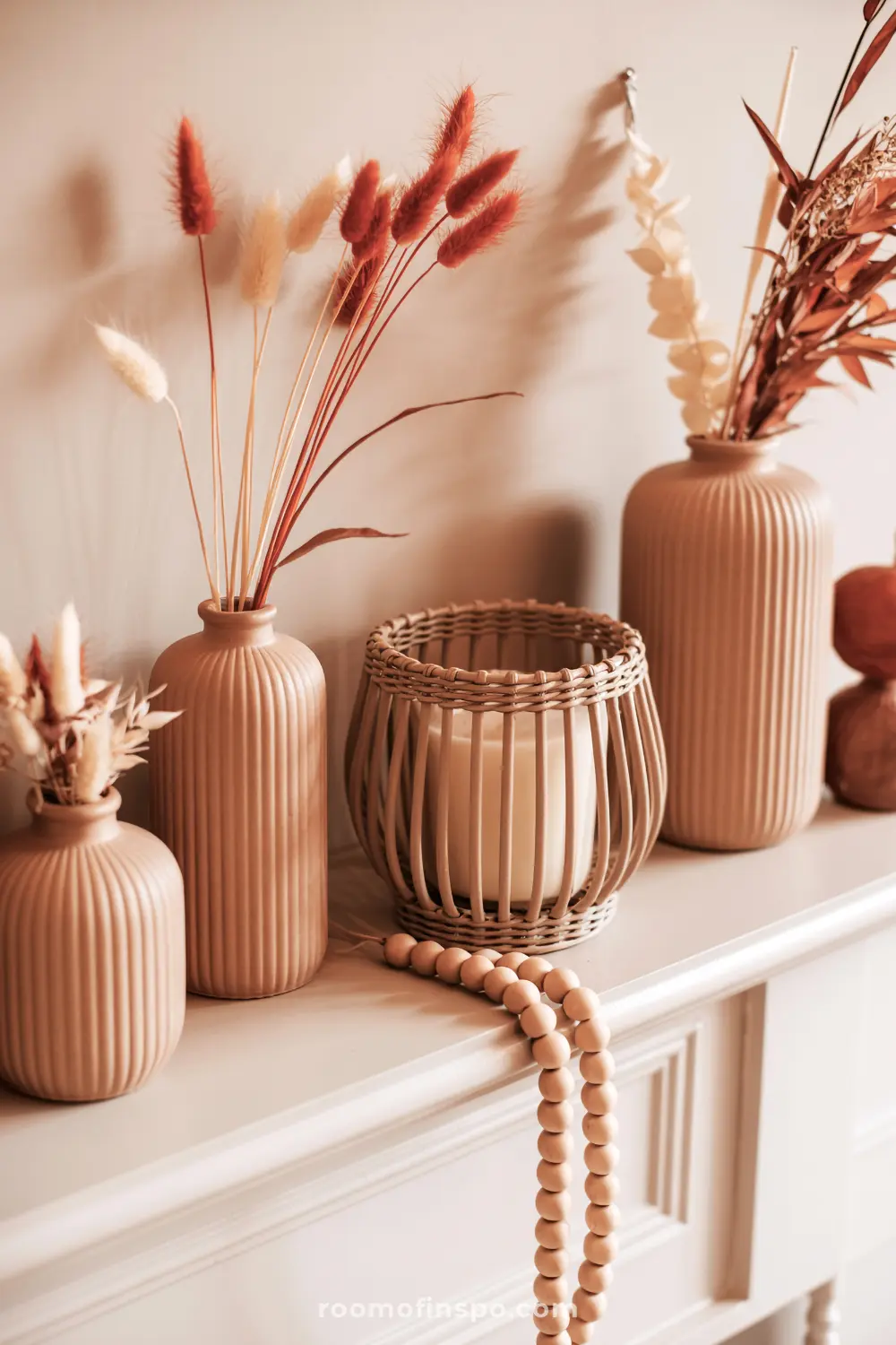 A stylish fall mantel showcases ribbed ceramic vases with dried grasses, a woven lantern with a candle, and wooden beads.