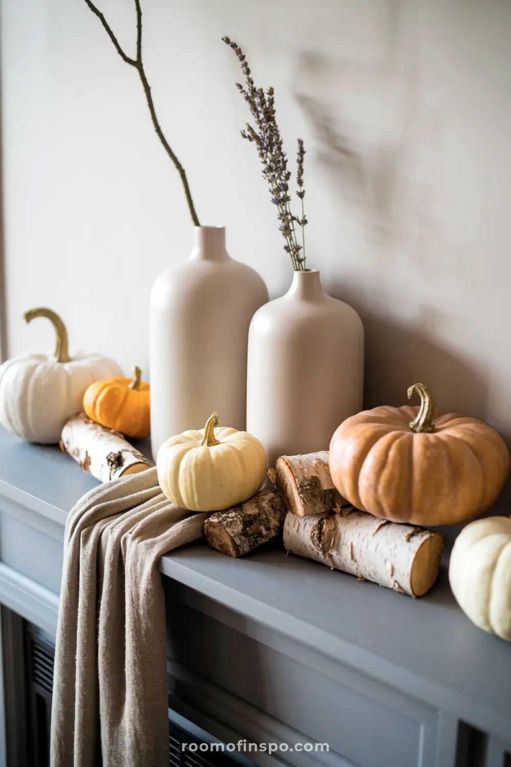 A chic fall mantel showcases various pumpkins, birch logs, and neutral vases with branches, creating a minimalist autumn display.