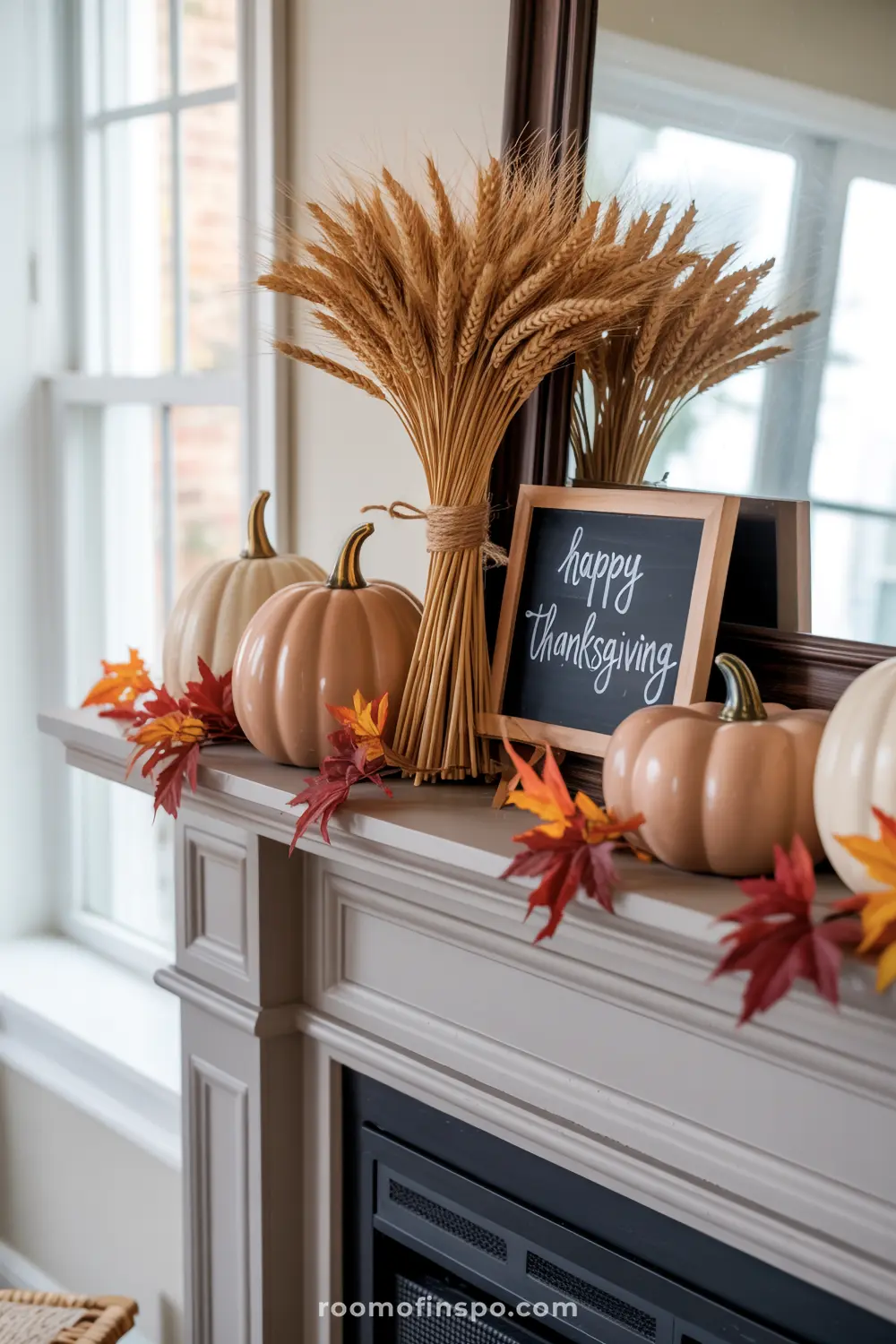 A fireplace mantel displays festive fall home decor with pumpkins, a bundle of wheat, colorful autumn leaves, and a "Happy Thanksgiving" sign.