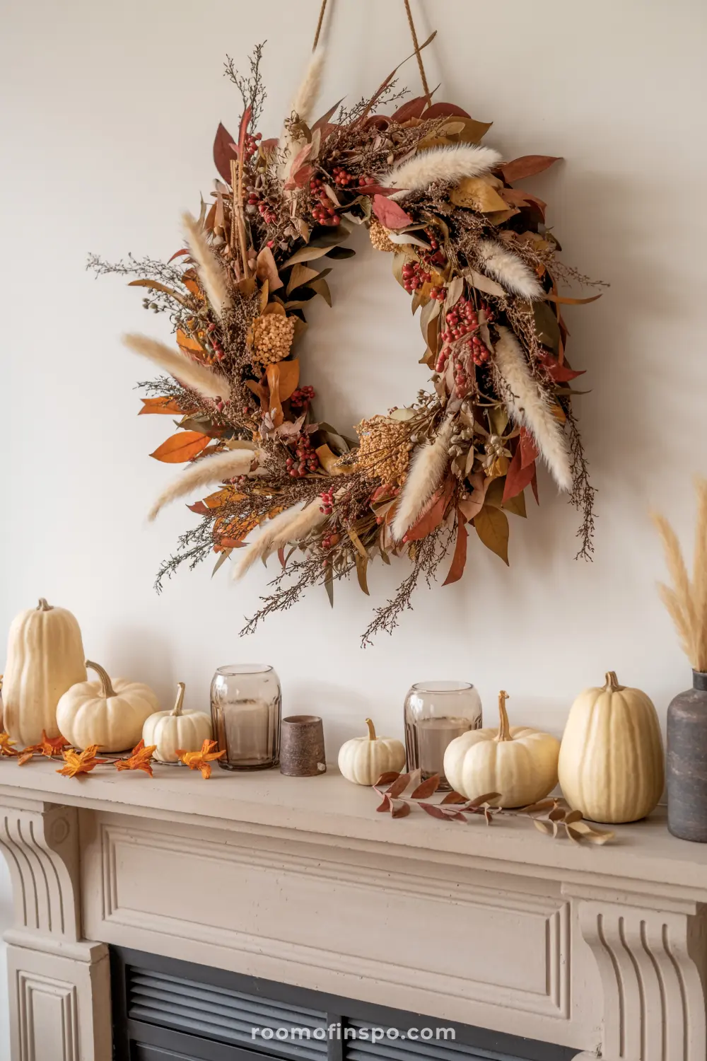 A cozy fall mantel is decorated with an array of white pumpkins, glass votives, and scattered autumn leaves, complemented by a large wreath.