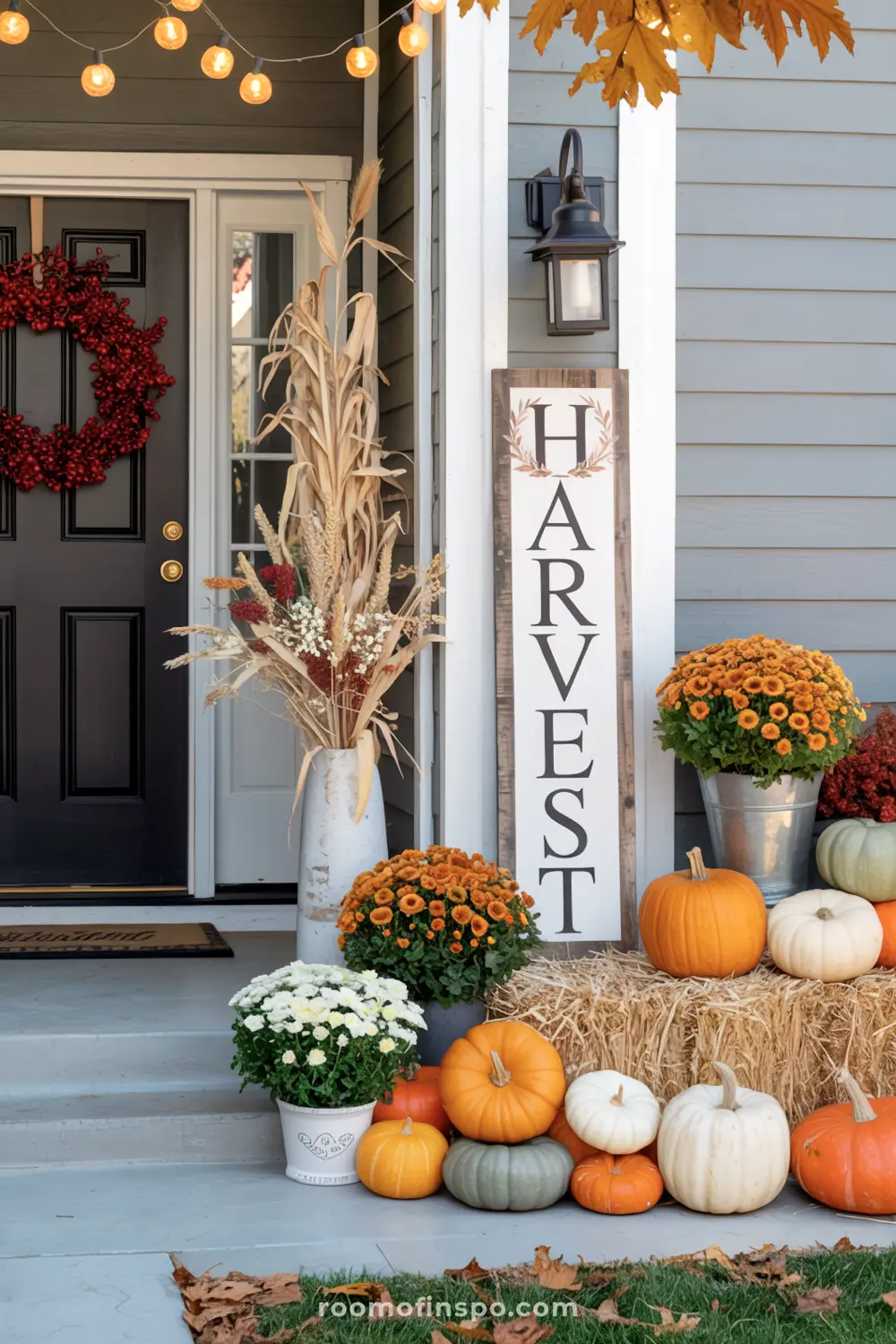 A charming fall front porch showcases "Harvest" decor, pumpkins, mums, and dried stalks, celebrating the autumn season.