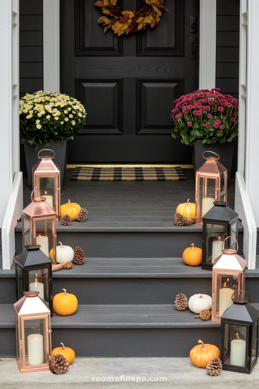 Lanterns, pumpkins, and mums line the steps of a dark front porch, creating a welcoming fall autumn display.