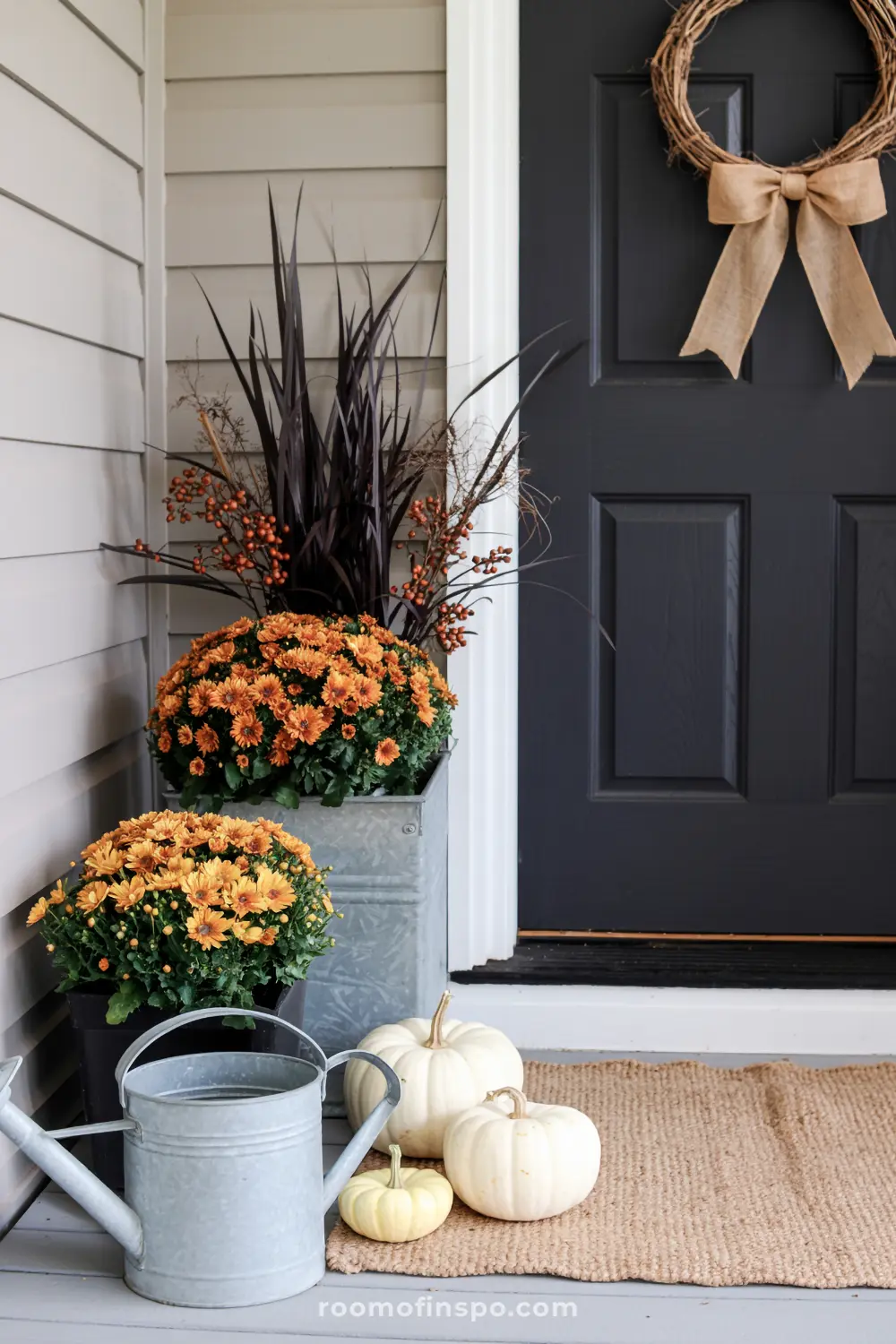 Potted red mums and pumpkins adorn a rustic fall front porch, inviting relaxation on a bright autumn day.
