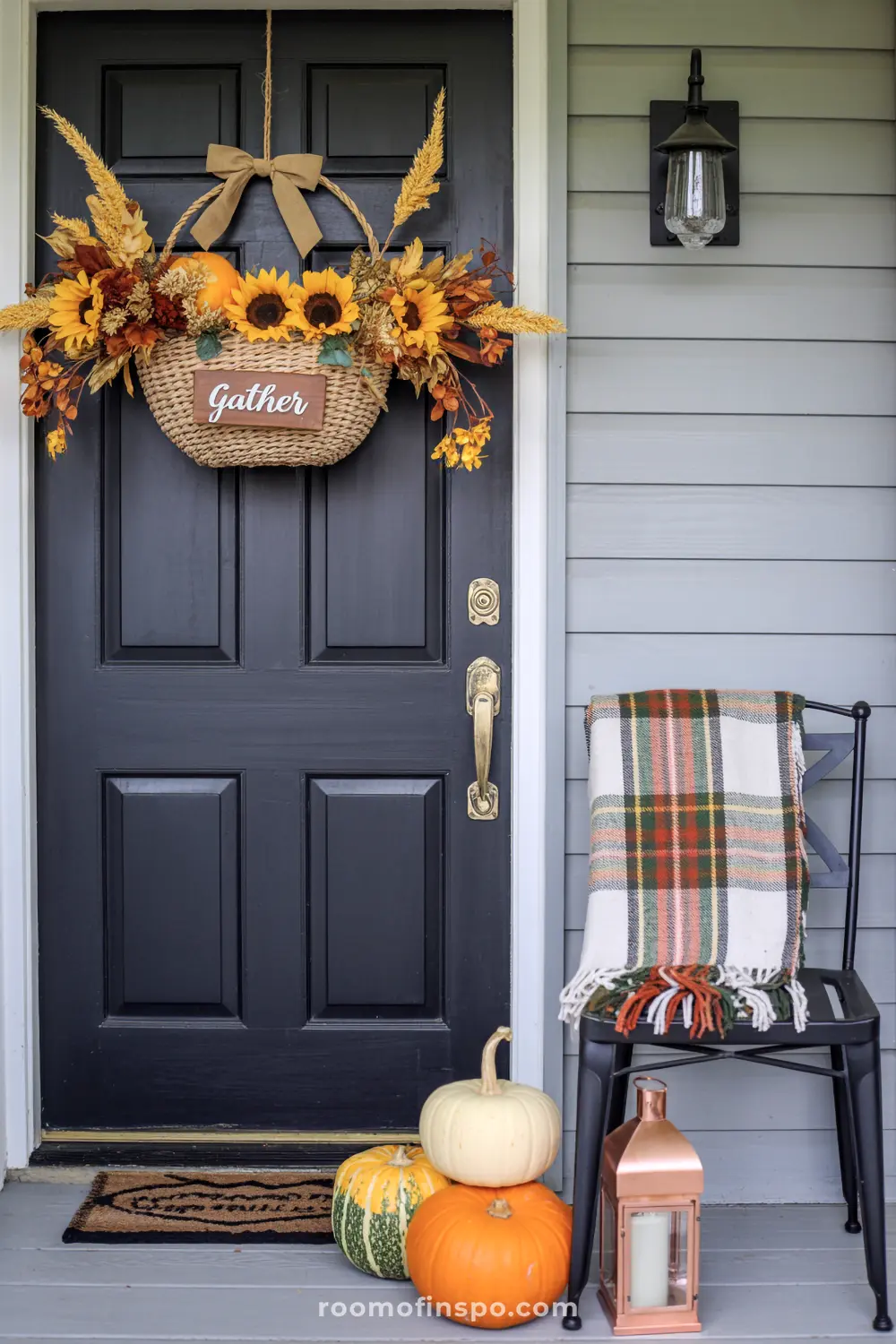 A detailed autumn front porch with a hanging basket of sunflowers and wheat, pumpkins, and plaid accents.