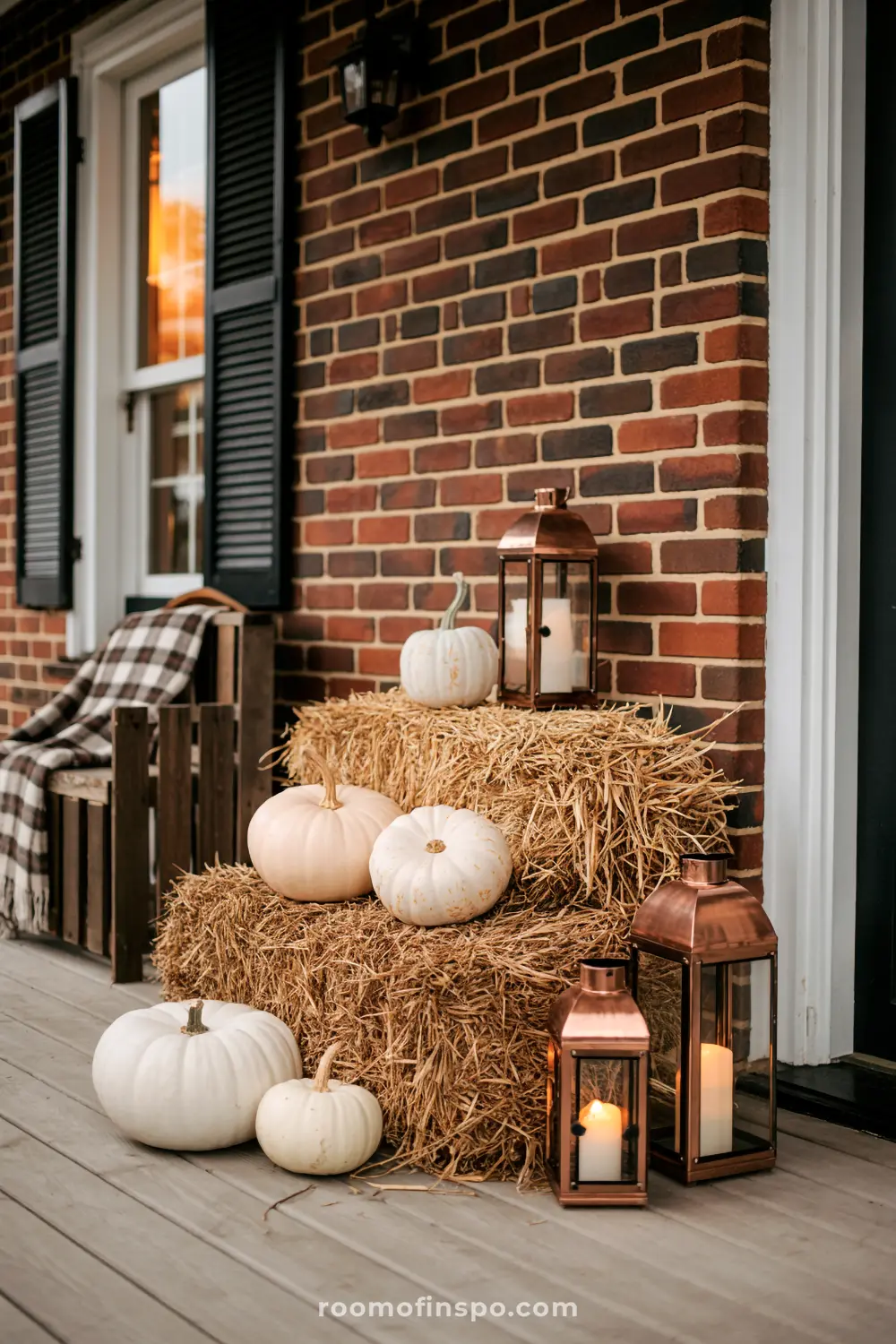 White pumpkins and glowing lanterns sit on hay bales, creating a rustic fall front porch scene for autumn.